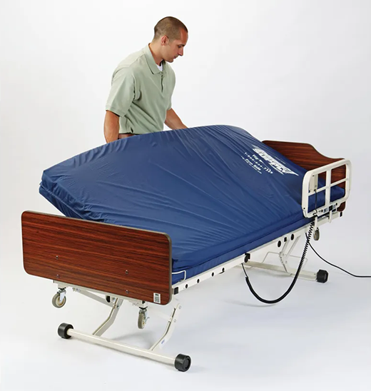 A man with short hair and wearing a polo shirt sets a blue mattress into a hospital bed frame