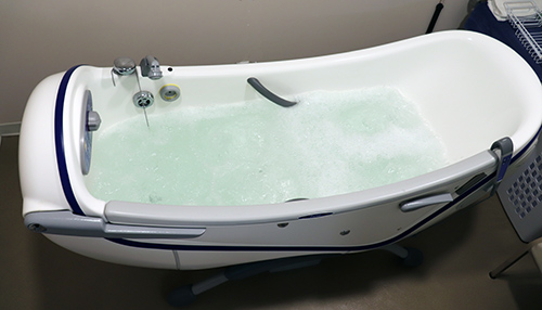 water bubbles in a curved whirlpool bathtub with grab bars and a hand-held sprayer fastened to the side.
