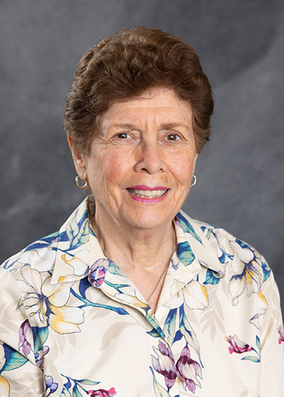 woman with short reddish-brown hair wearing a cream blouse with pink and blue flower design